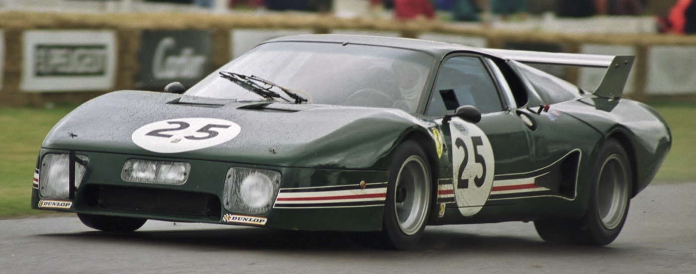 Dark green Ferrari 512 BB LM with white number 25 roundels and a rear wing, driven along the hill course past straw bales