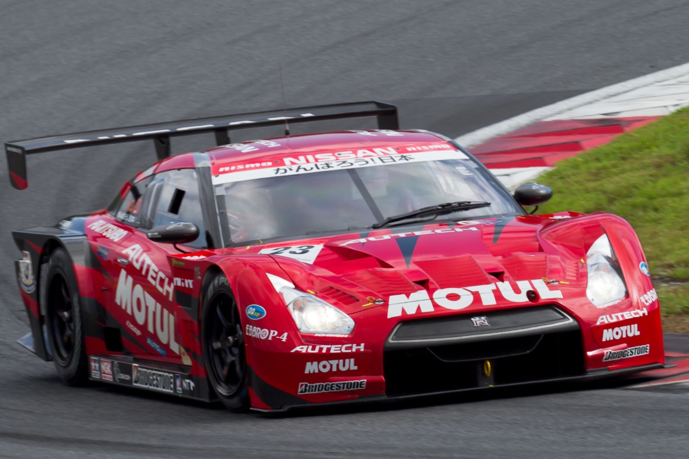 Red Motul Autech Nissan GT-R GT500 racing car number 23 cornering at Fuji Speedway, its rear wing and Motul lettering prominent