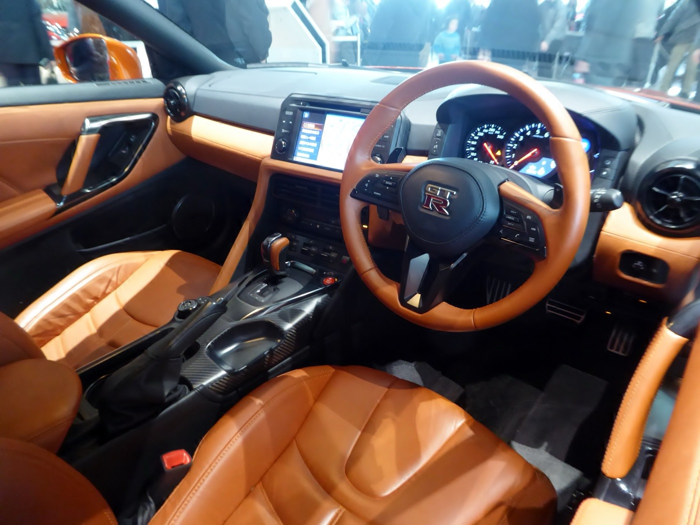 Right-hand-drive Nissan GT-R cabin with tan leather seats, dashboard and steering wheel, a carbon-fibre centre console and an 8-inch touchscreen