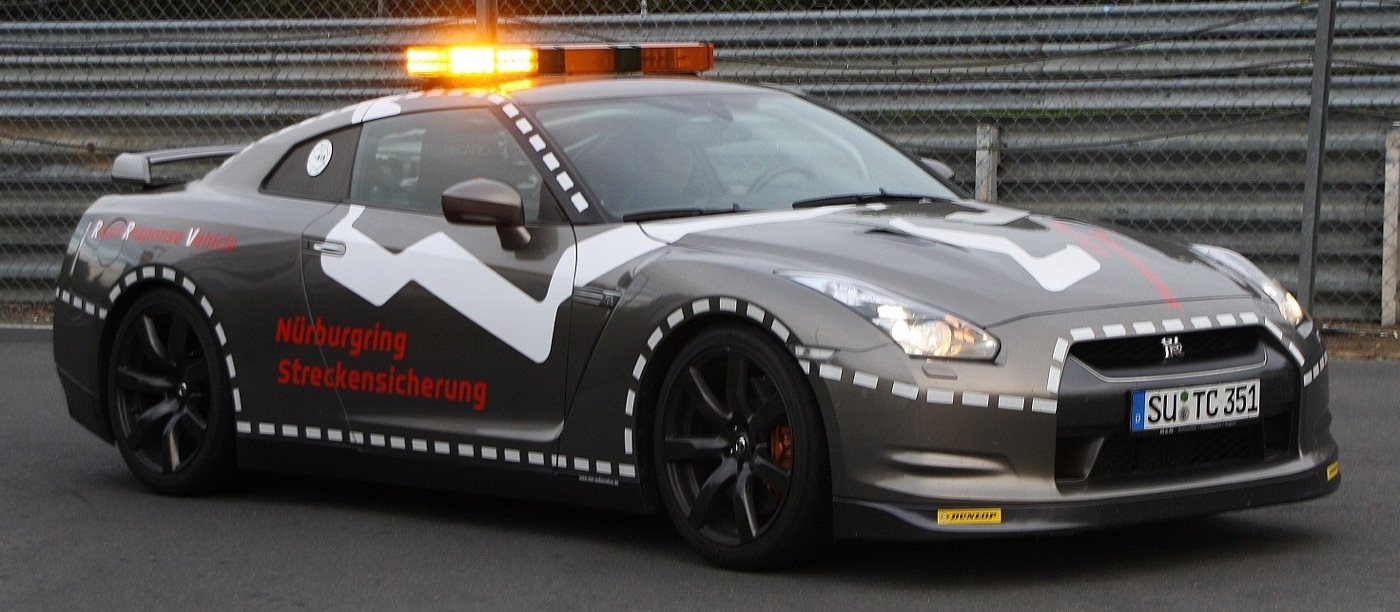 Grey Nissan GT-R with an orange light bar and Nürburgring Streckensicherung lettering, parked by the track barrier