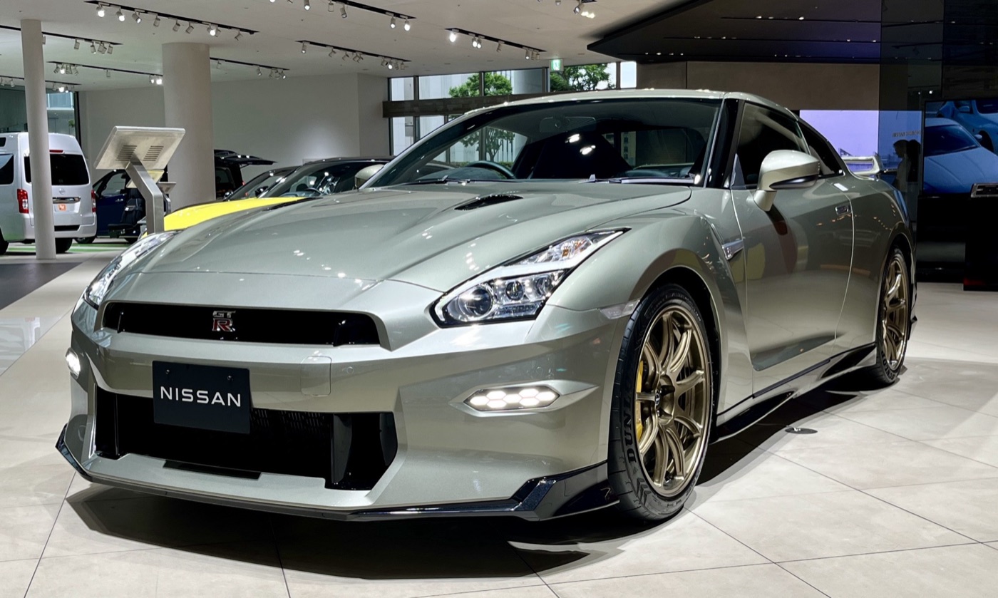 Pale green Nissan GT-R T-spec of the 2024 model year with bronze wheels and the final front bumper, in a showroom