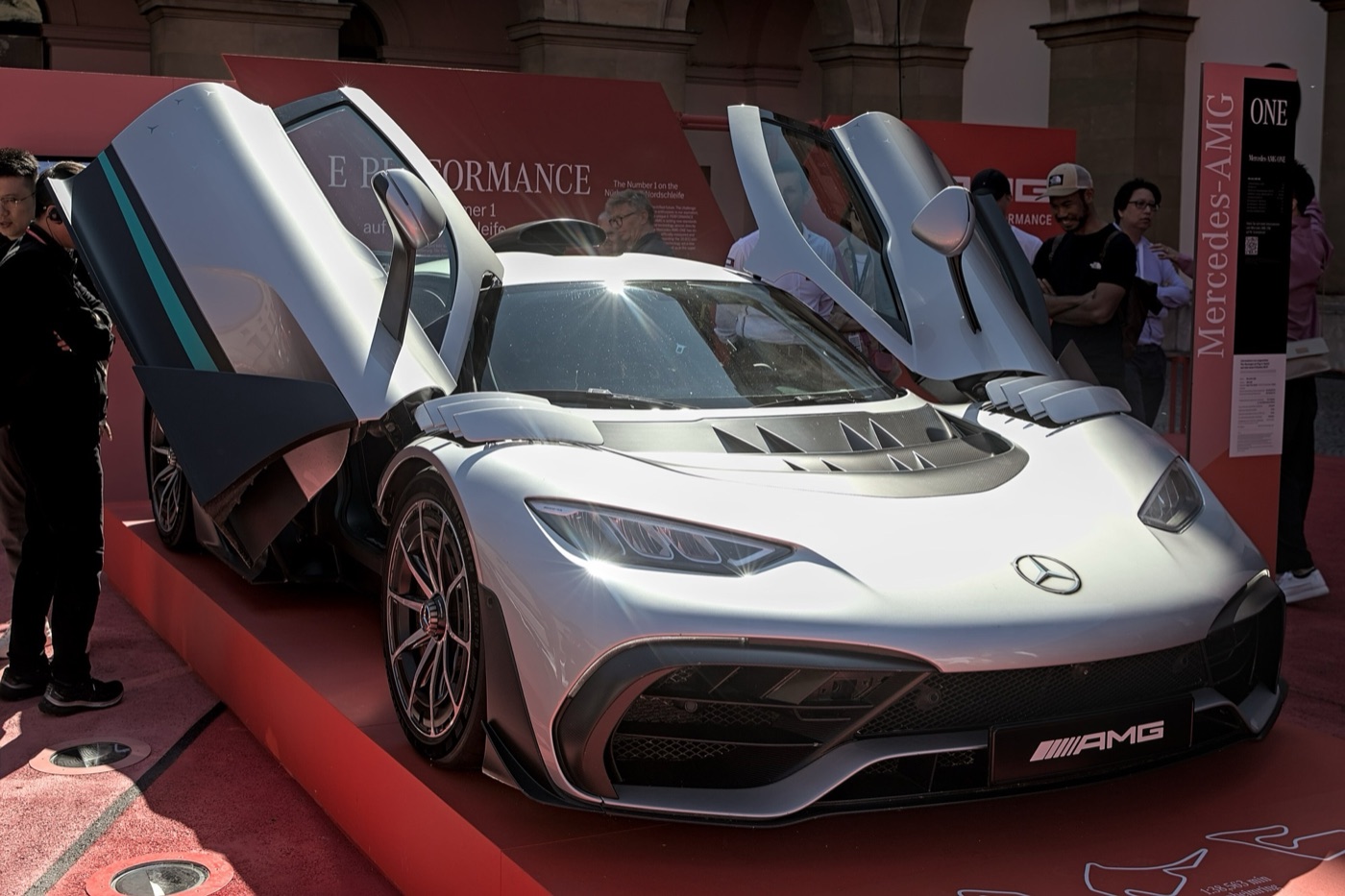 Silver and black Mercedes-AMG ONE hypercar with both doors raised on a red show stand