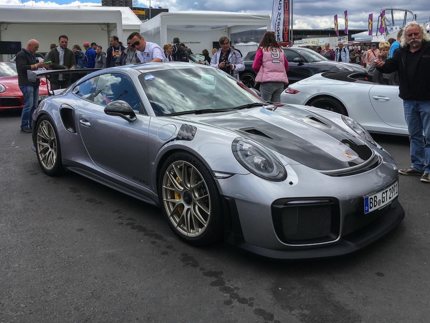 Silver Porsche 911 GT2 RS of the 991 generation with a carbon bonnet and gold wheels, parked among visitors in a paddock