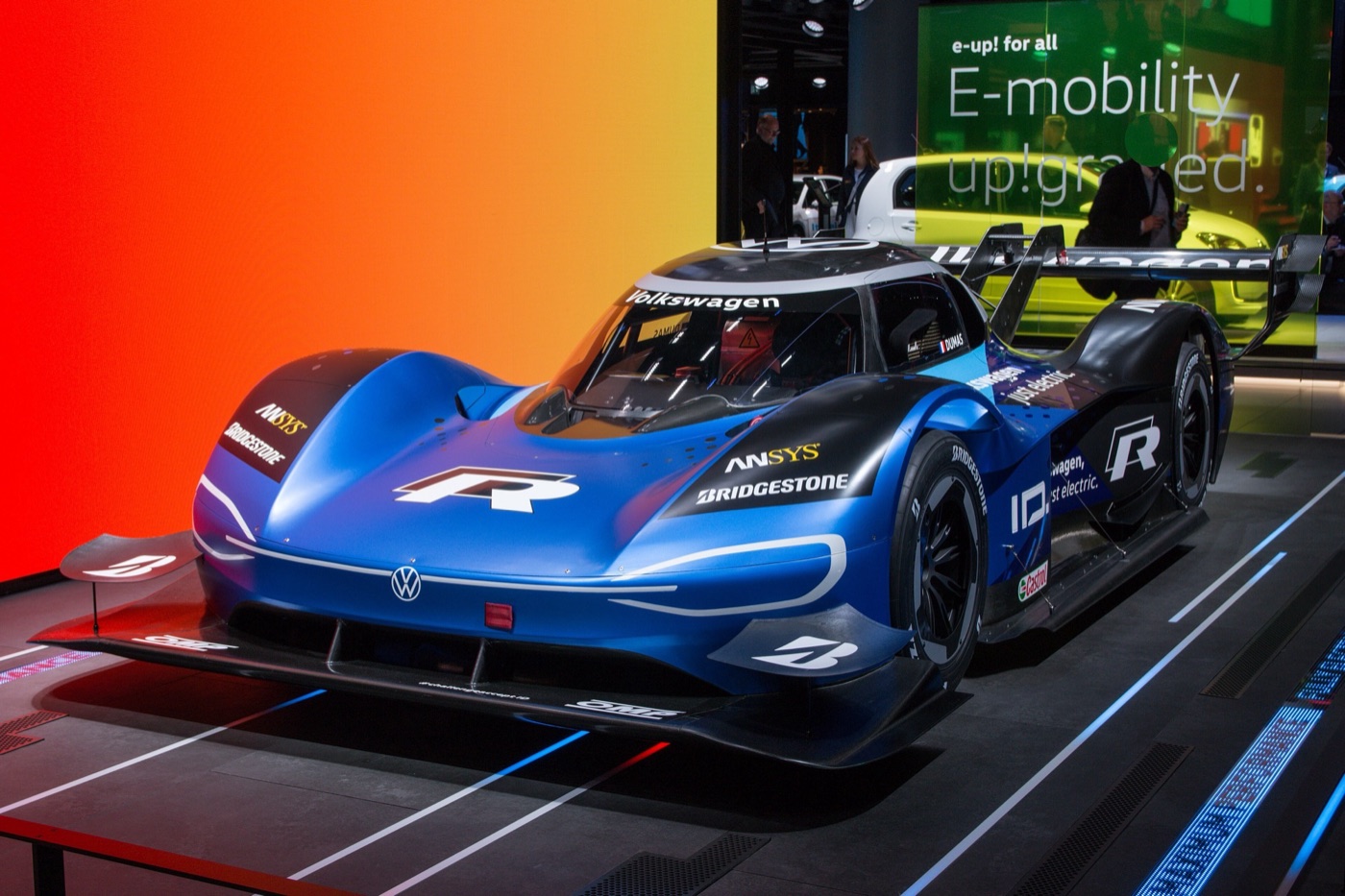 The blue and black Volkswagen ID.R electric racing car with its large rear wing on a show stand