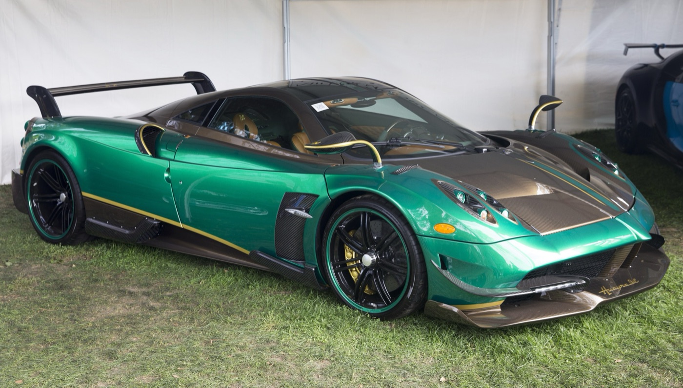 Green Pagani Huayra BC with a large rear wing, carbon front splitter and gold-edged black wheels, parked on grass