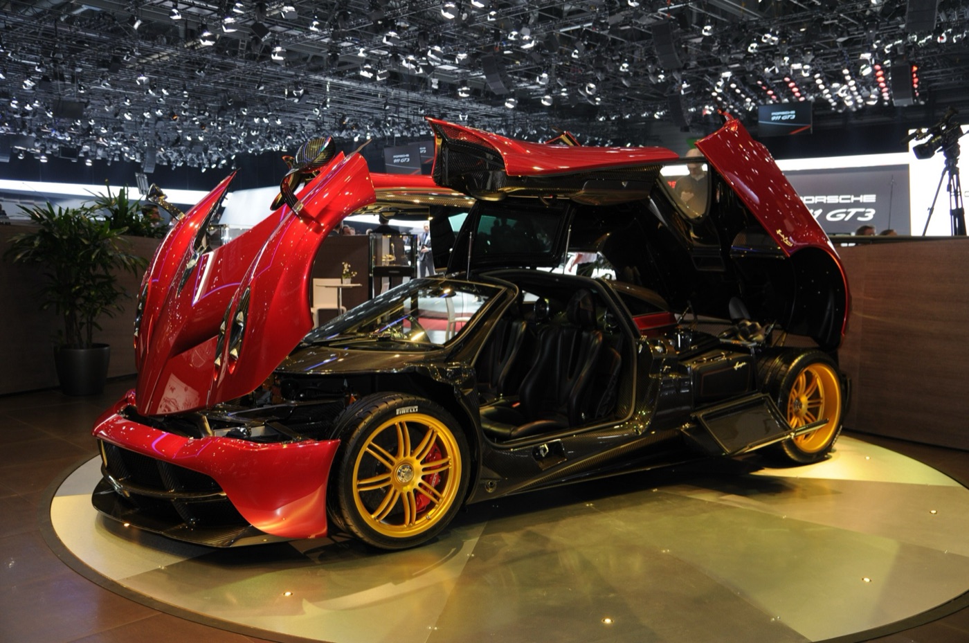 Red and carbon Pagani Huayra with its gullwing doors, front clamshell and engine cover all raised on a motor show stand