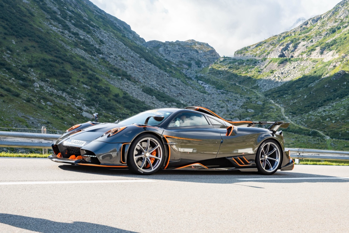 Dark carbon Pagani Imola with orange trim and a large rear wing, parked on an Alpine pass road