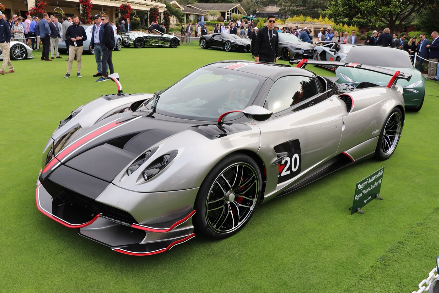 Silver and carbon Pagani Huayra Roadster BC with red trim and a fixed rear wing, displayed on a lawn