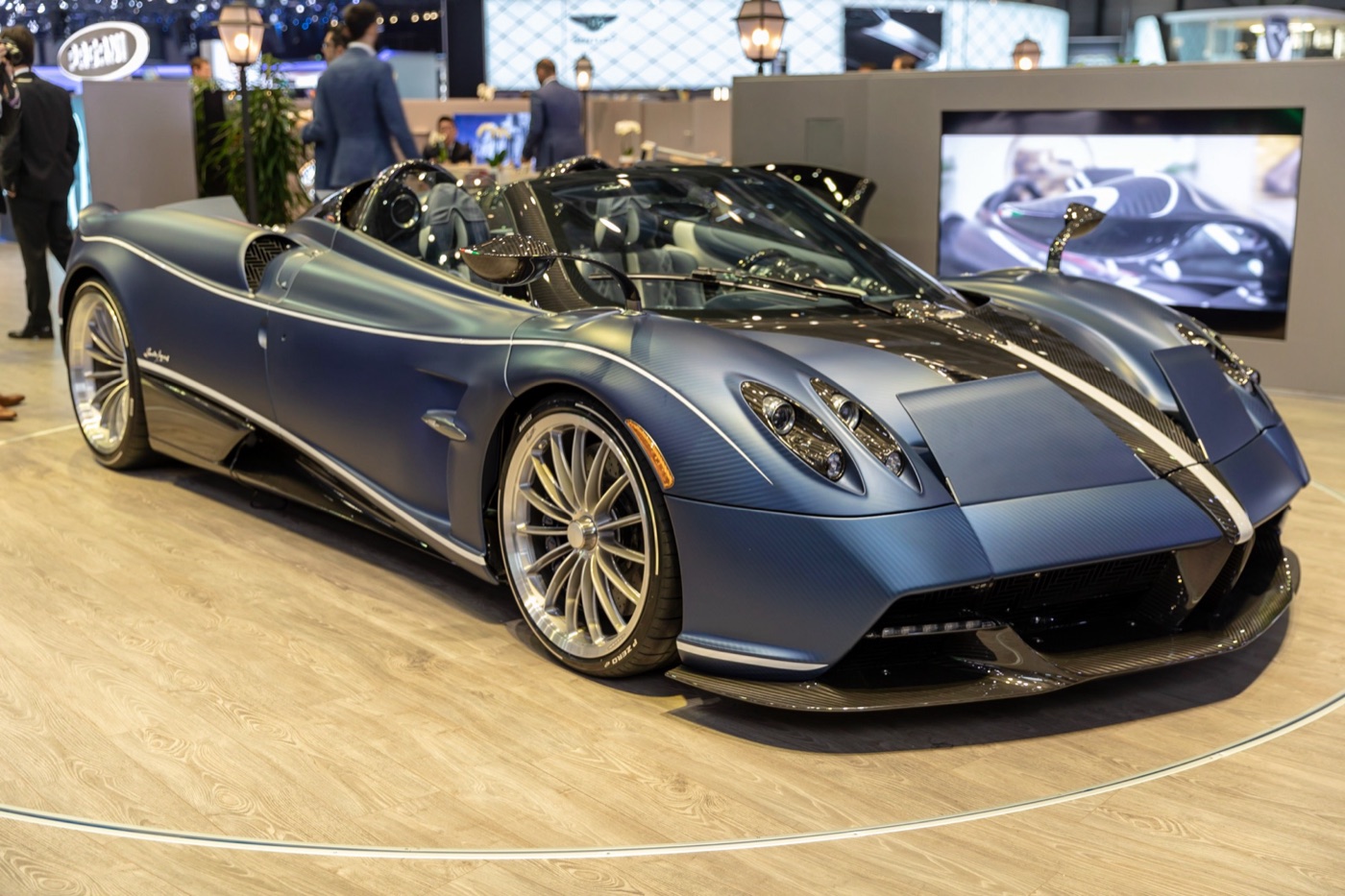 Blue-grey Pagani Huayra Roadster with its roof removed and white pinstripes, on a motor show stand