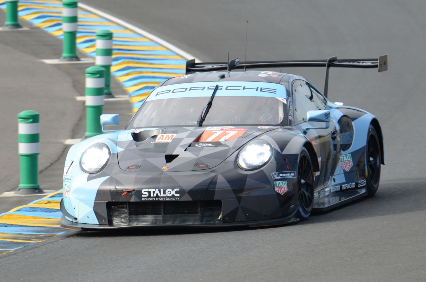 The blue and grey No. 77 Dempsey-Proton Racing Porsche 911 RSR between the green bollards of a Le Mans chicane