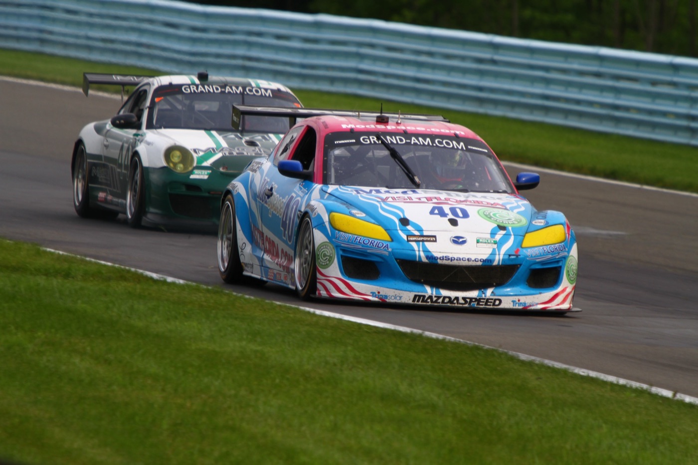 The blue and white No. 40 Dempsey Racing Mazda RX-8 ahead of a green and white Porsche 911 at Watkins Glen