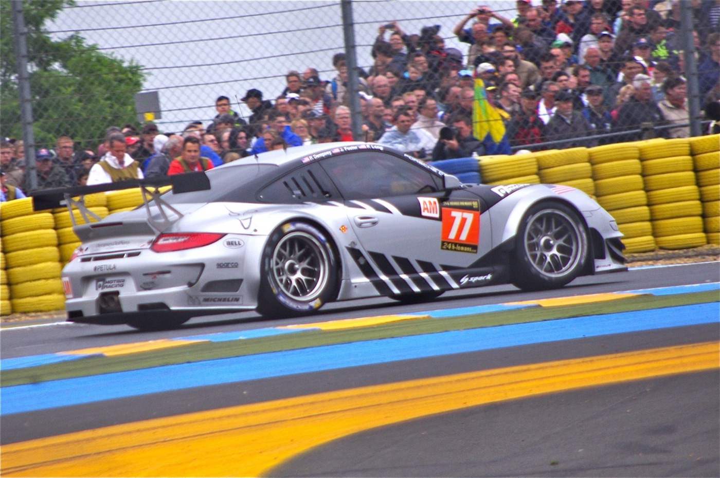 The silver and black No. 77 Porsche 911 GT3 RSR passing a packed spectator fence at Le Mans