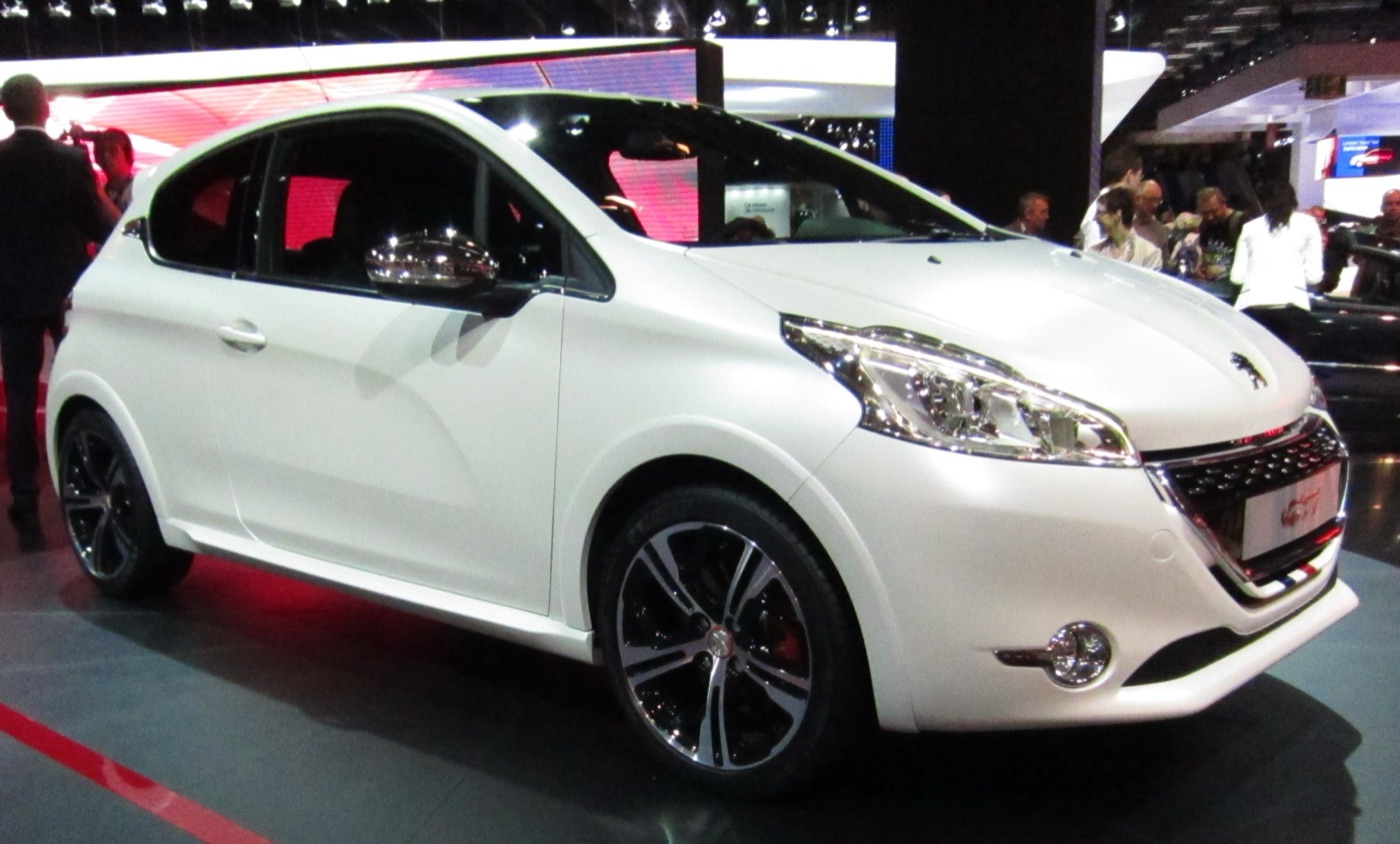 White Peugeot 208 GTi three-door with dark two-tone alloy wheels and red brake calipers on a motor show stand
