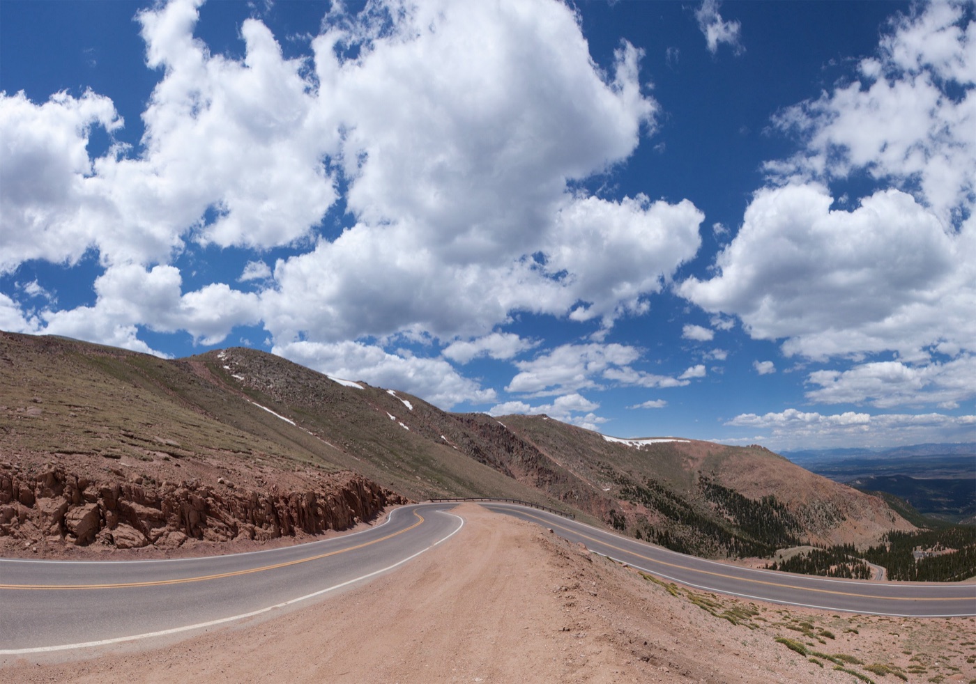 Pikes Peak Highway curving across a bare, red-brown mountainside above the treeline under a sky of white clouds