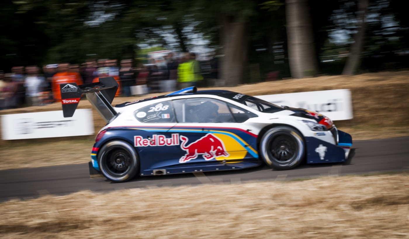 Peugeot 208 T16 Pikes Peak in Red Bull livery with race number 208 and a large rear wing, at speed past a crowd