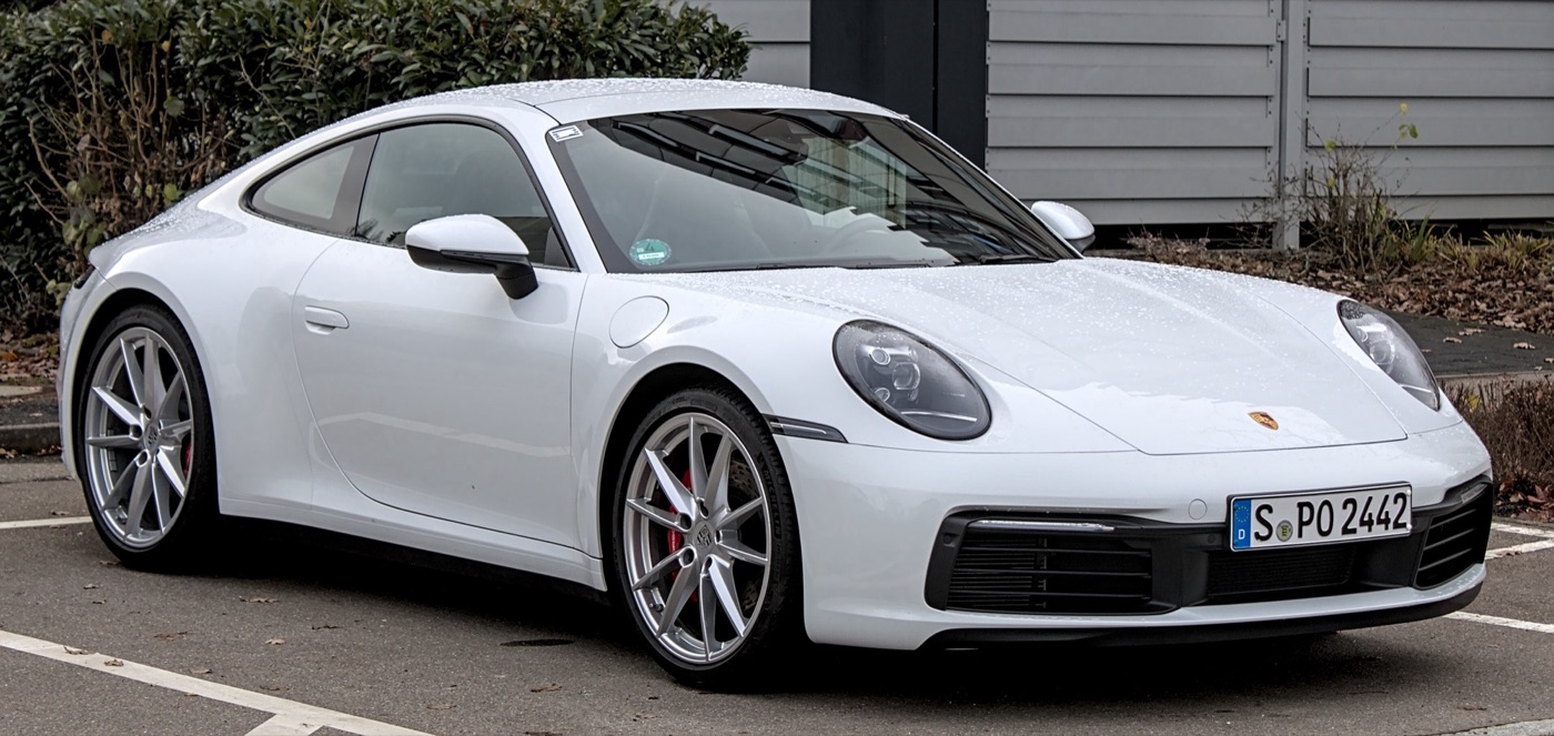 White Porsche 992 Carrera S coupé, the eighth-generation 911, parked in front of a hedge