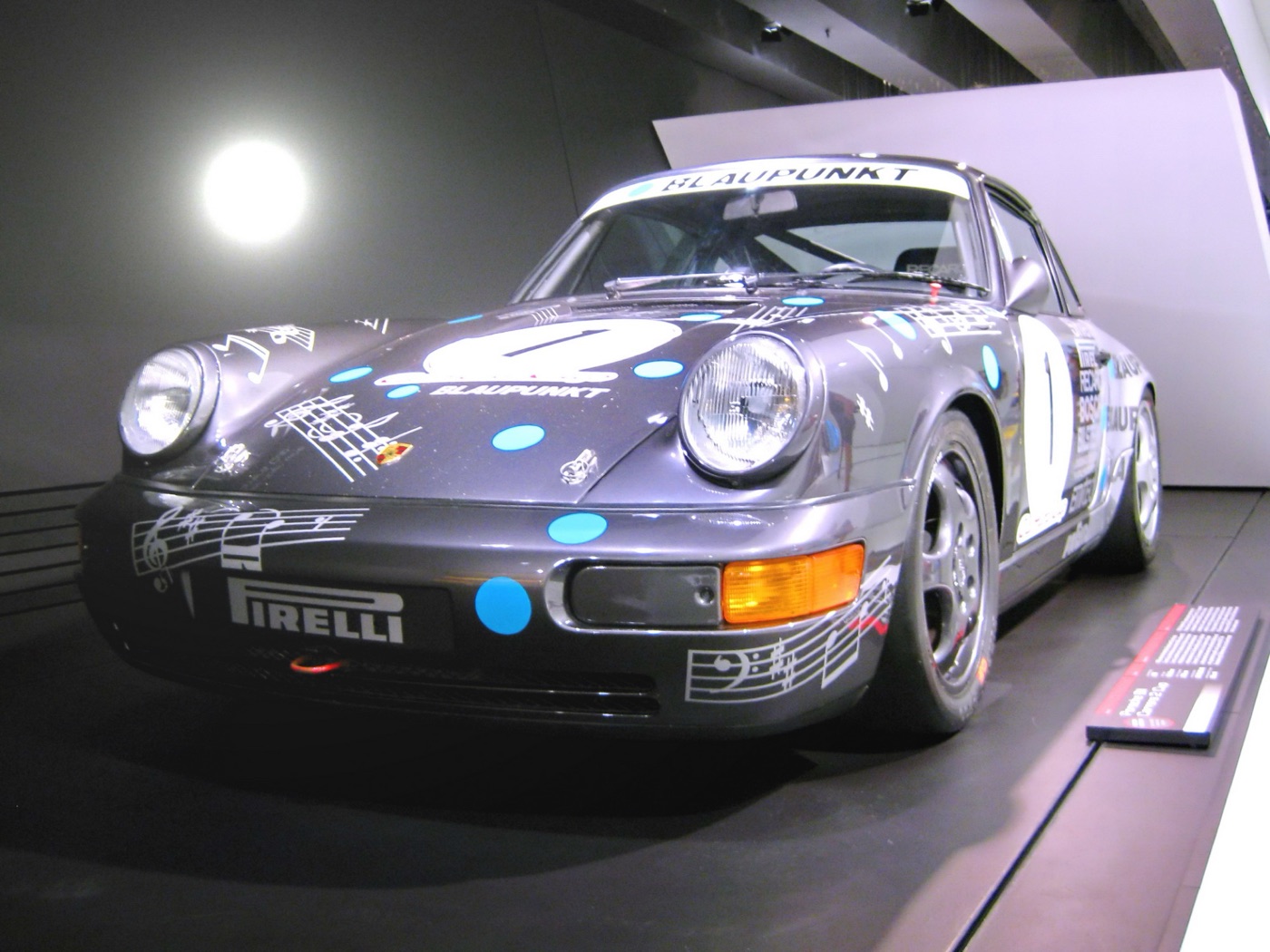 Grey 964-generation Porsche 911 Carrera 2 Cup in Blaupunkt livery with race number 1, on display in the Porsche Museum