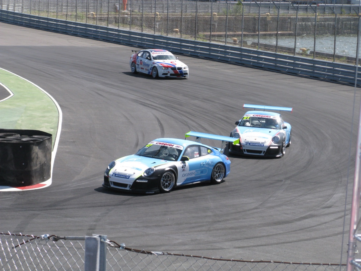 Two 997-generation Porsche 911 GT3 Cups in blue, white and black racing through a hairpin, with a BMW M3 on the same stretch of track
