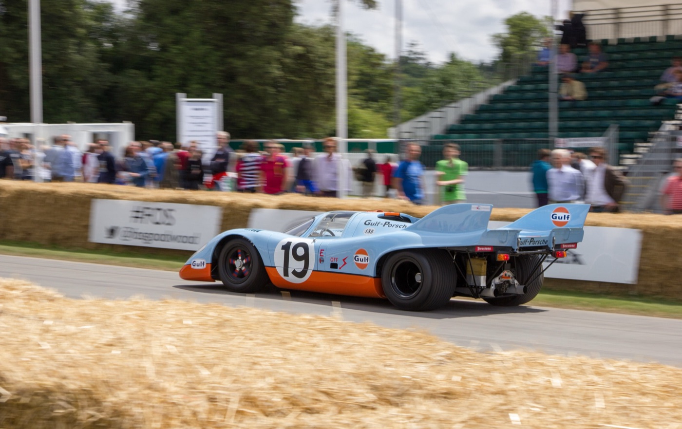 Light blue and orange Gulf Porsche 917K number 19 with tail fins passing hay bales at Goodwood