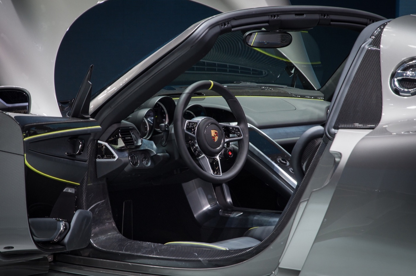 Interior of a Porsche 918 Spyder seen through the open door: three-spoke steering wheel with a rotary mode switch, carbon sills and acid-green trim lines