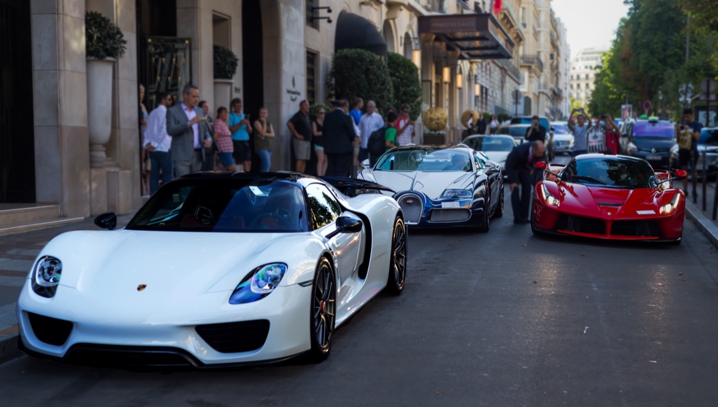 White Porsche 918 Spyder in the foreground, a blue and white Bugatti Veyron and a red LaFerrari behind on a Paris street