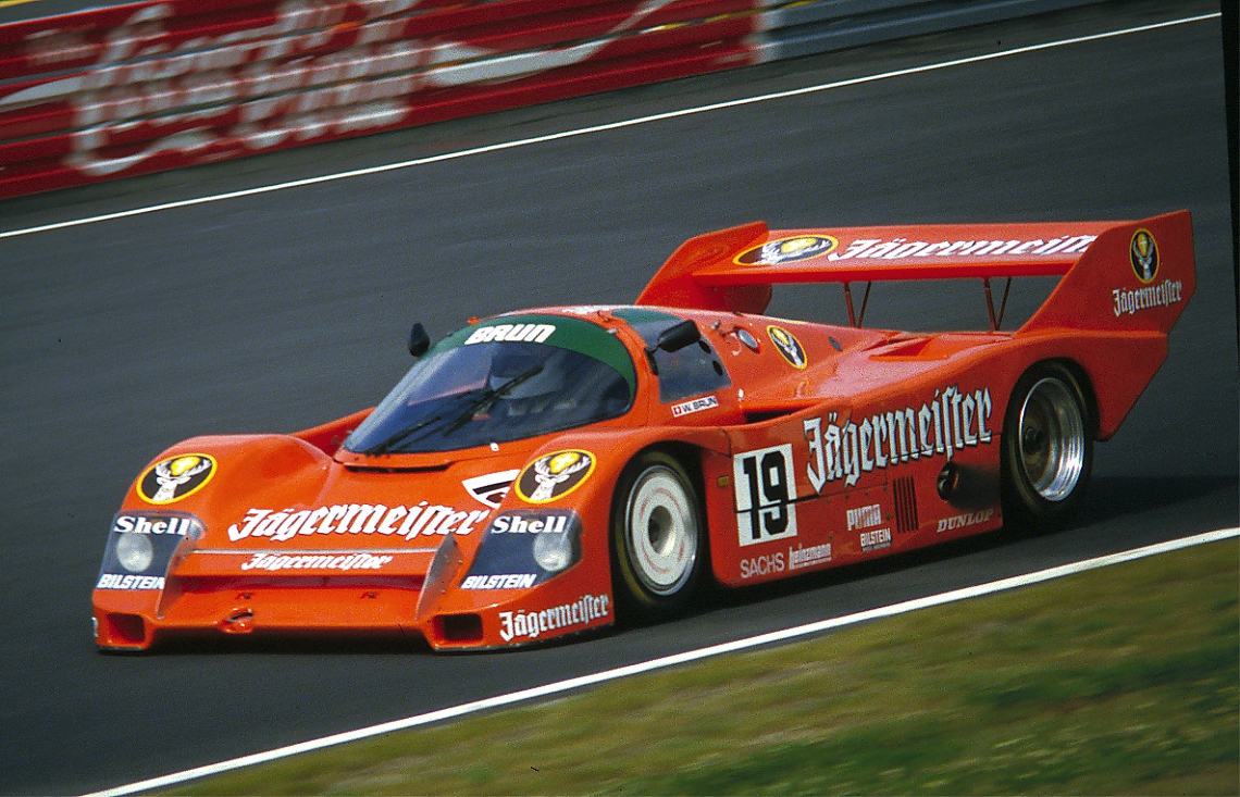 Orange Jägermeister-liveried Porsche 956 number 19 with a high rear wing on a racing circuit