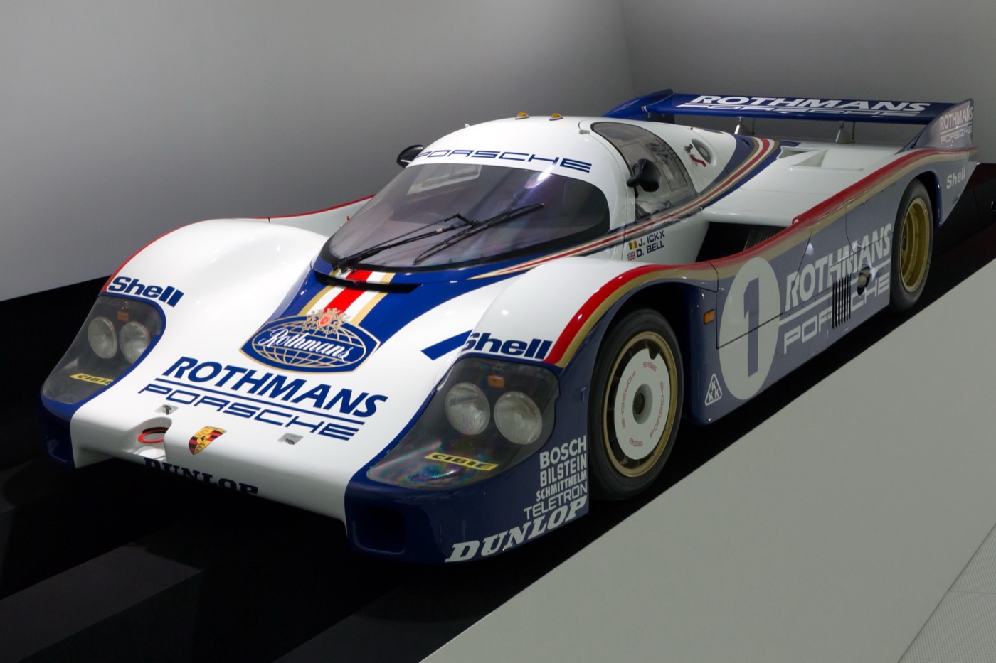 White, blue and red Rothmans Porsche 956 number 1 on a display plinth, seen from the front left