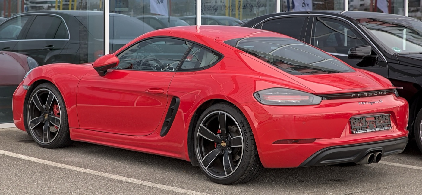 Red Porsche 718 Cayman S from the rear three-quarters, showing the black strip between its tail lights