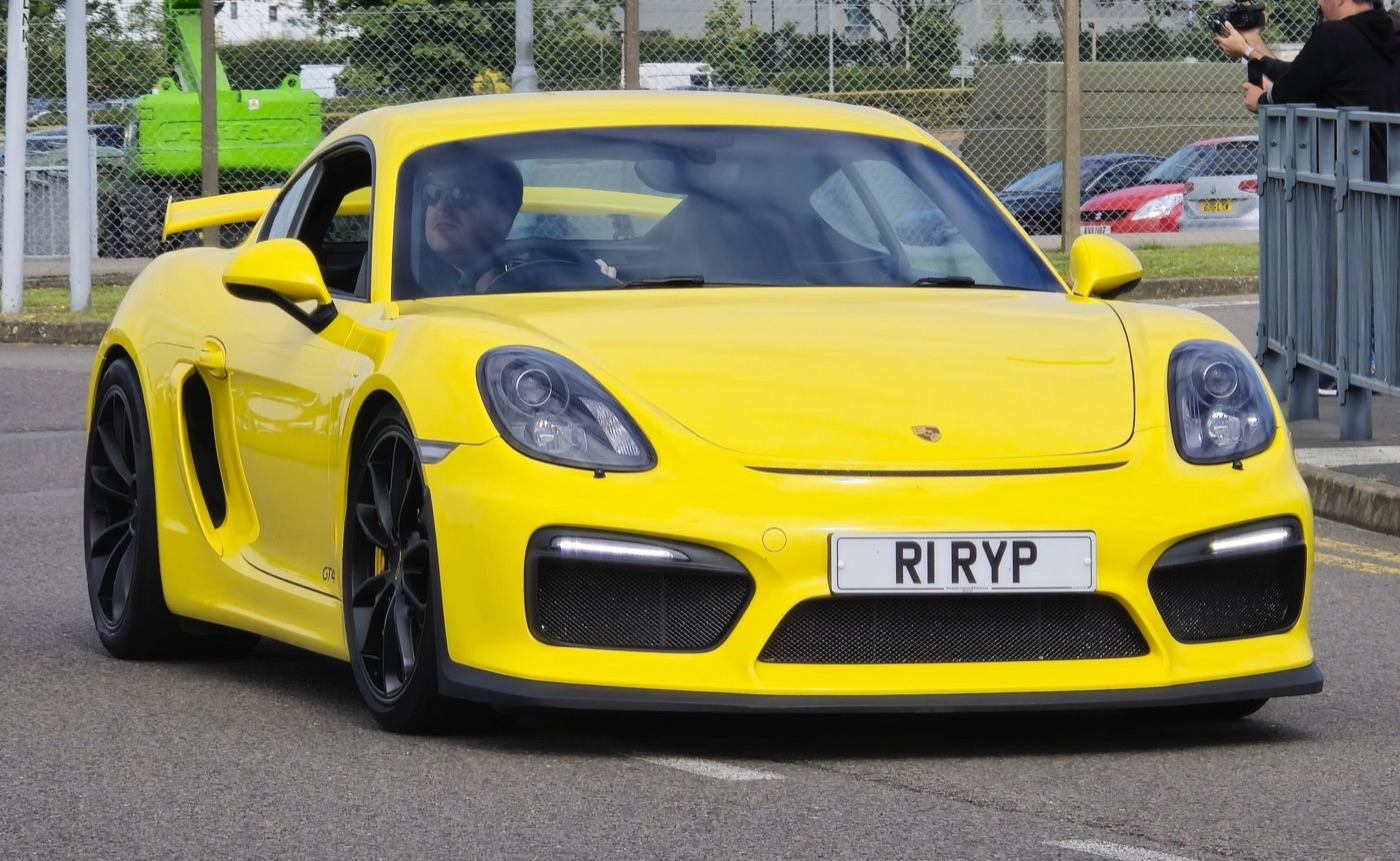 Yellow Porsche Cayman GT4 of the 981 series from the front, showing the three large air intakes and the rear wing above the roofline