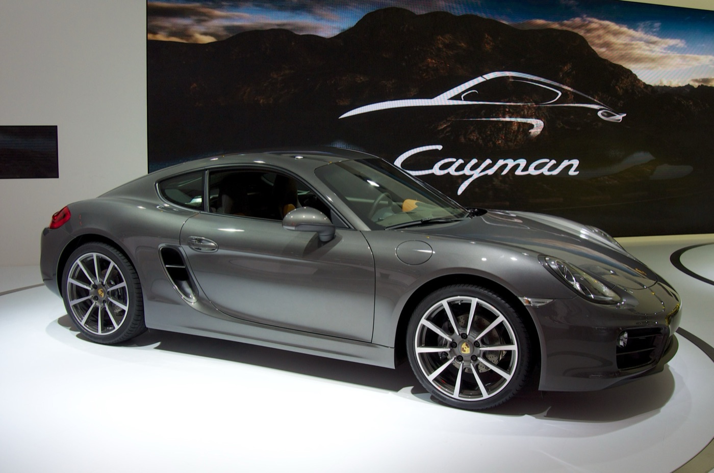 Grey Porsche Cayman 981 on Porsche’s stand at the 2012 Los Angeles Auto Show, with the Cayman name on the screen behind
