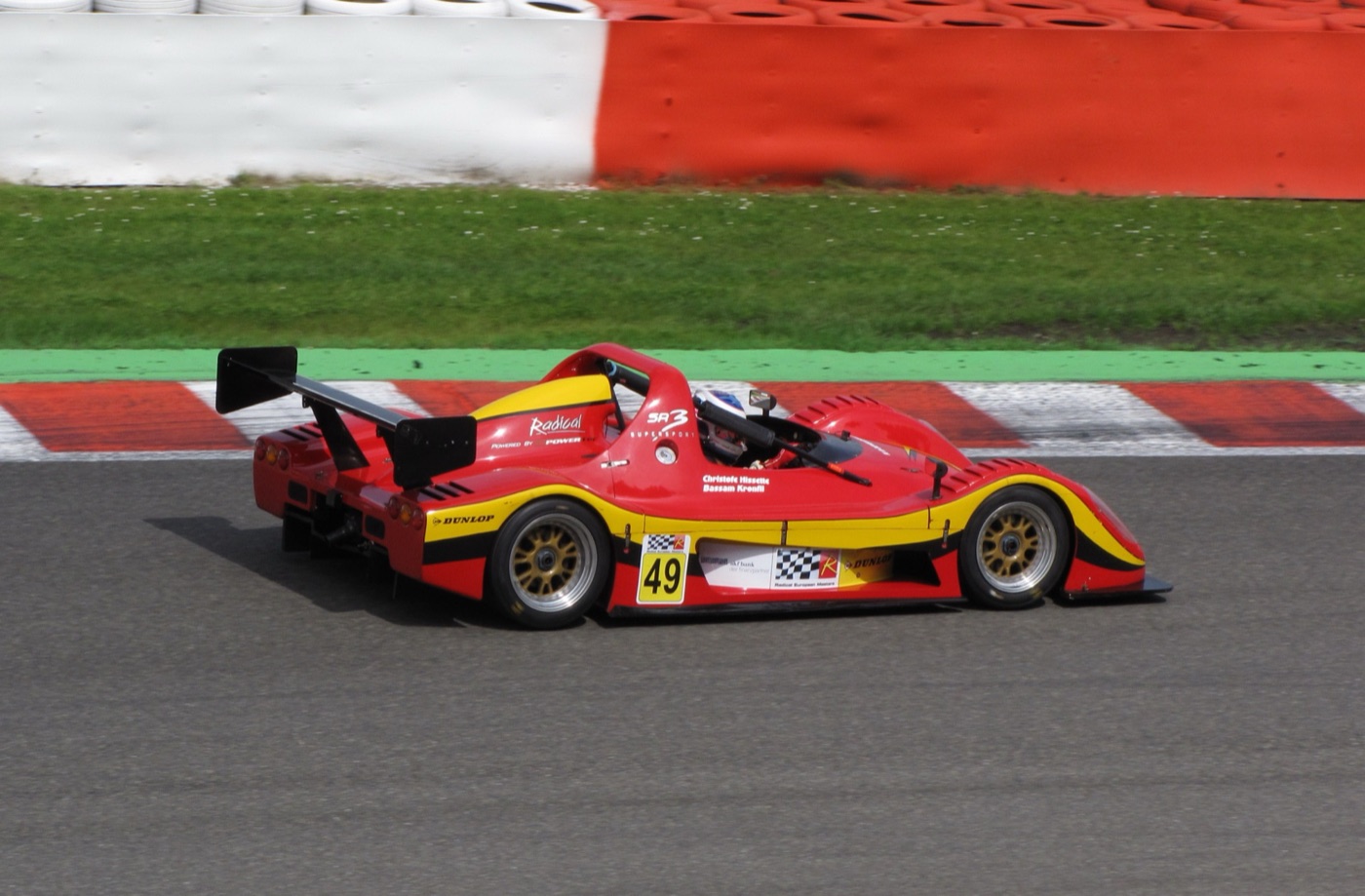 Red and yellow Radical SR3 number 49 racing past red and white kerbs at Spa-Francorchamps