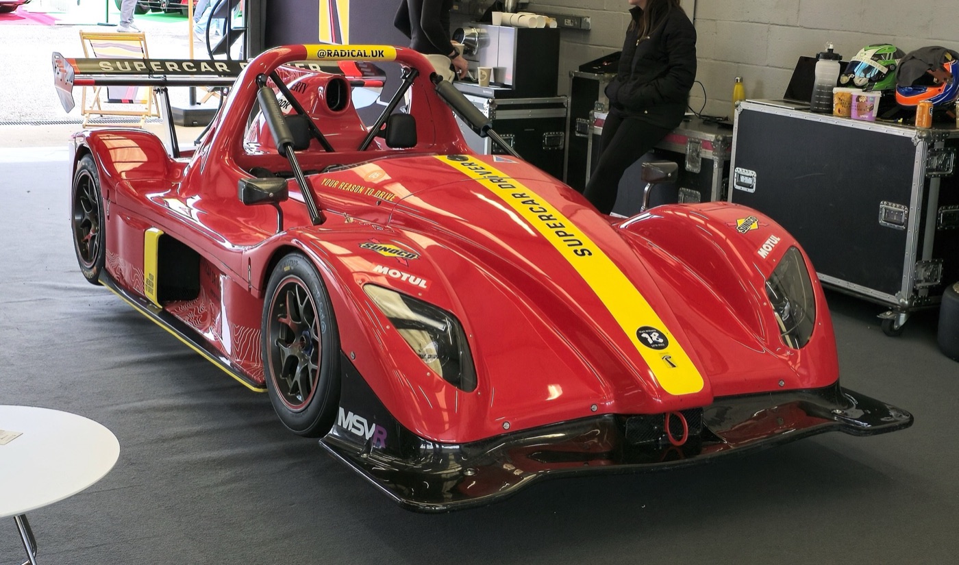 Red Radical SR3 XXR with a yellow stripe and a large rear wing, parked in a race garage