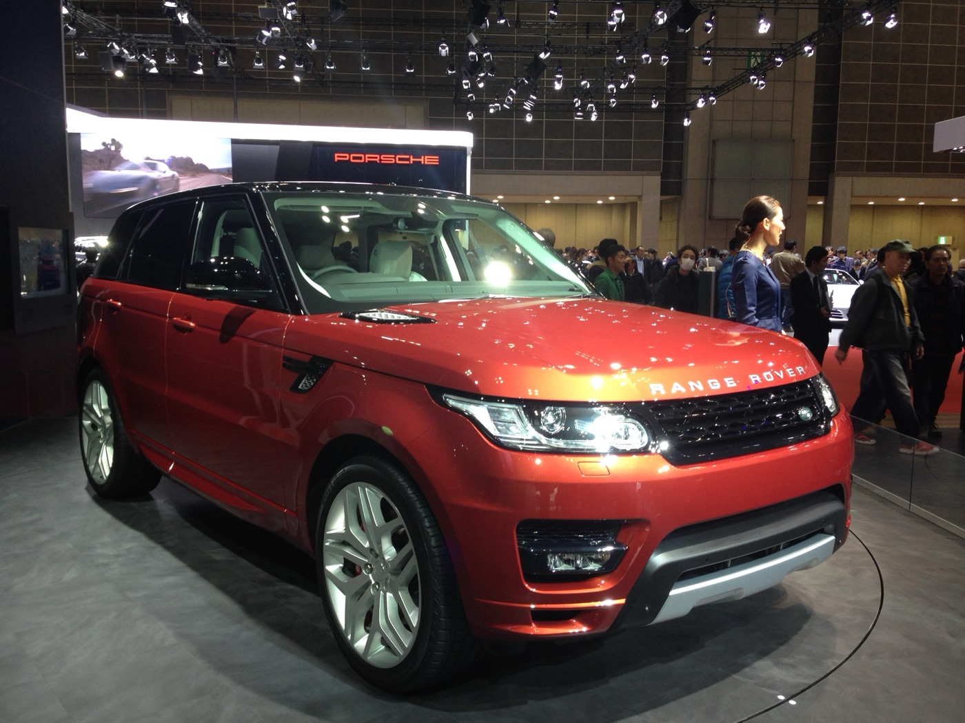 Orange Range Rover Sport L494 with a black roof on a turntable at the Tokyo Motor Show, crowds behind