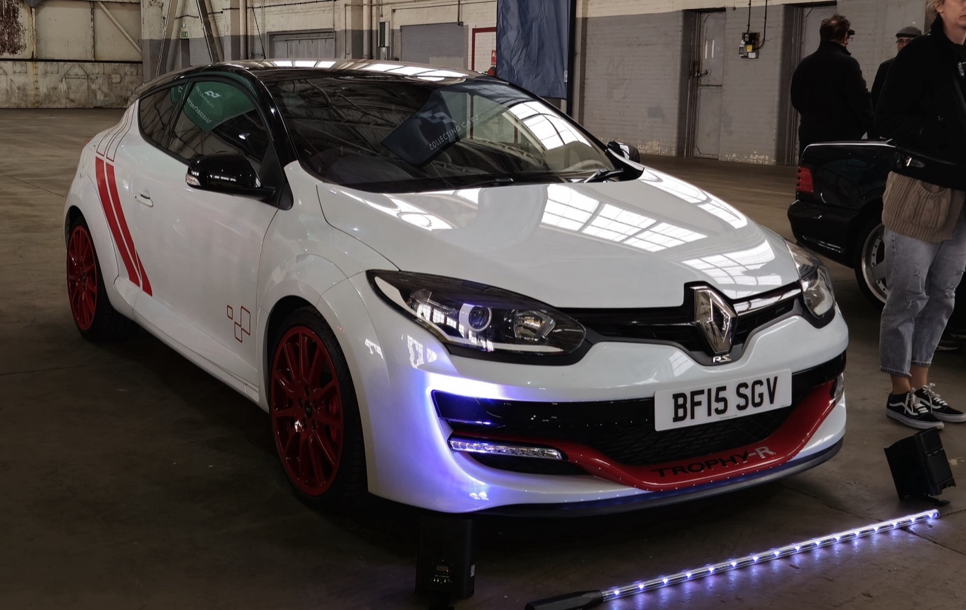 White Megane RS 275 Trophy-R with red wheels, red side stripes and a red Trophy-R front blade on display indoors