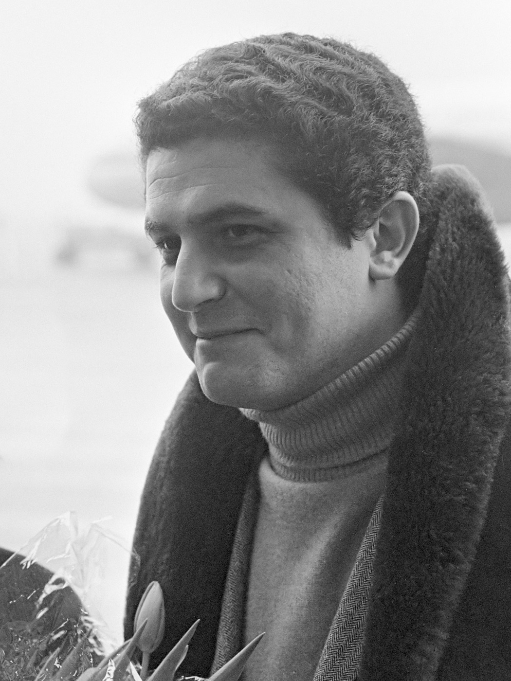 Black and white portrait of a young Claude Lelouch in a polo-neck jumper and a coat with a fur collar