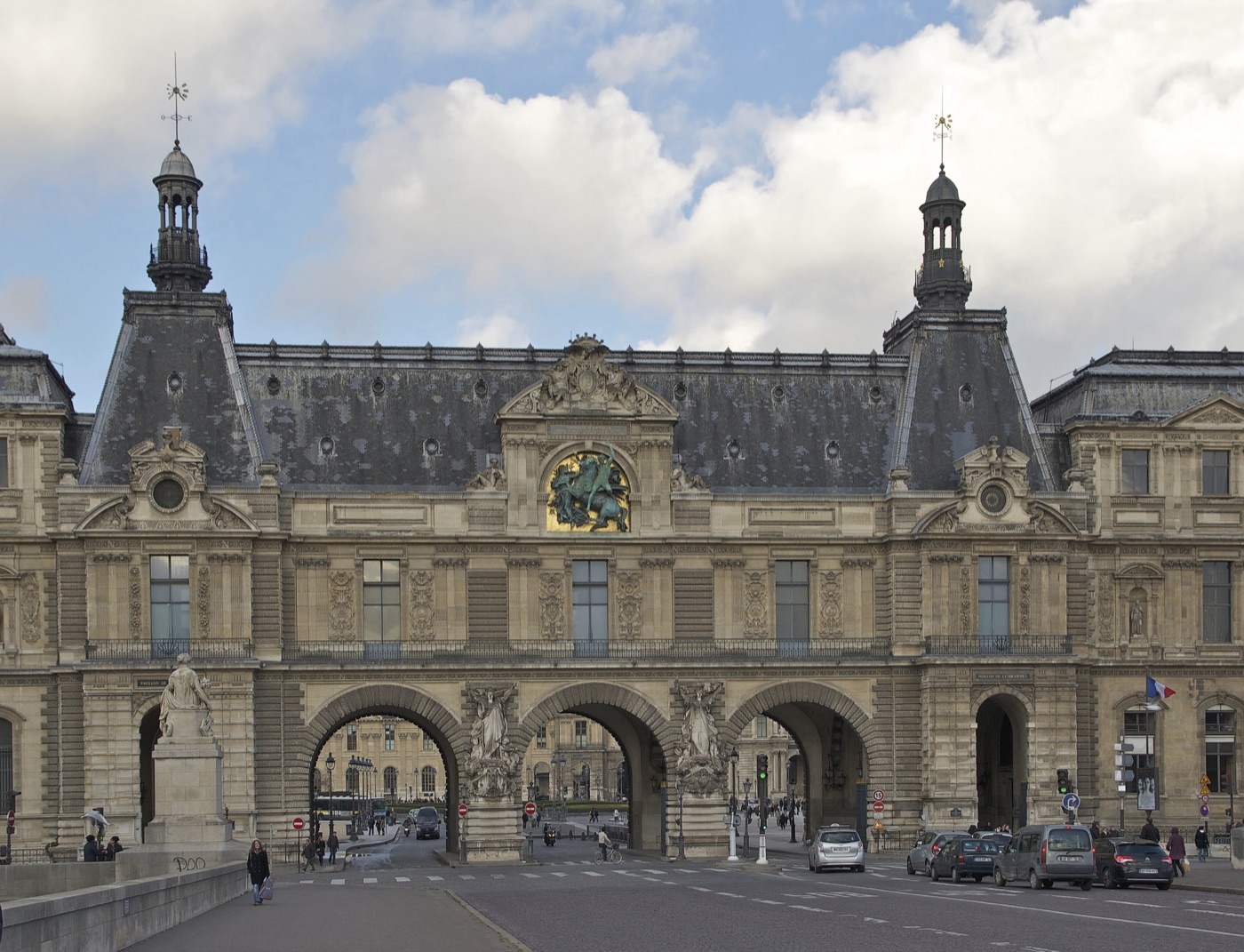 The three arches of the Guichets du Louvre, a wing of the Louvre palace, with cars and traffic lights on the road in front