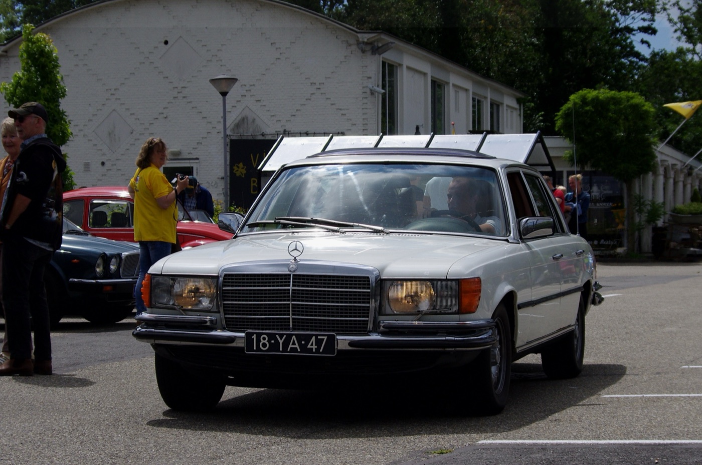 Front view of a white 1976 Mercedes-Benz 450 SEL 6.9 saloon with a chrome grille and amber indicators, at a classic car meeting