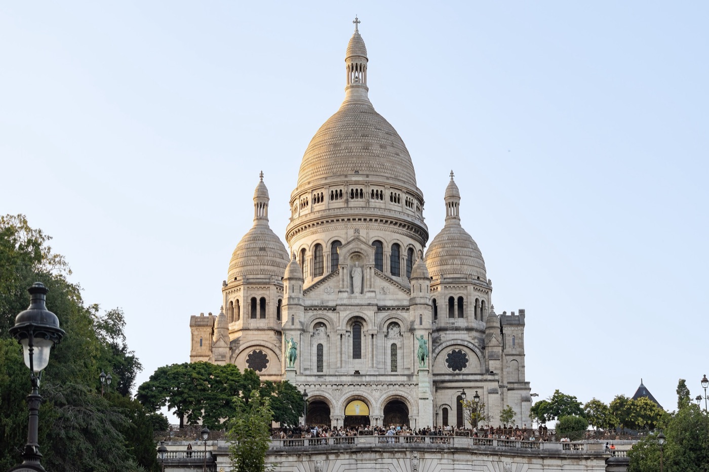 The white domes of the Sacré-Cœur basilica on Montmartre, seen from below the steps on a clear evening