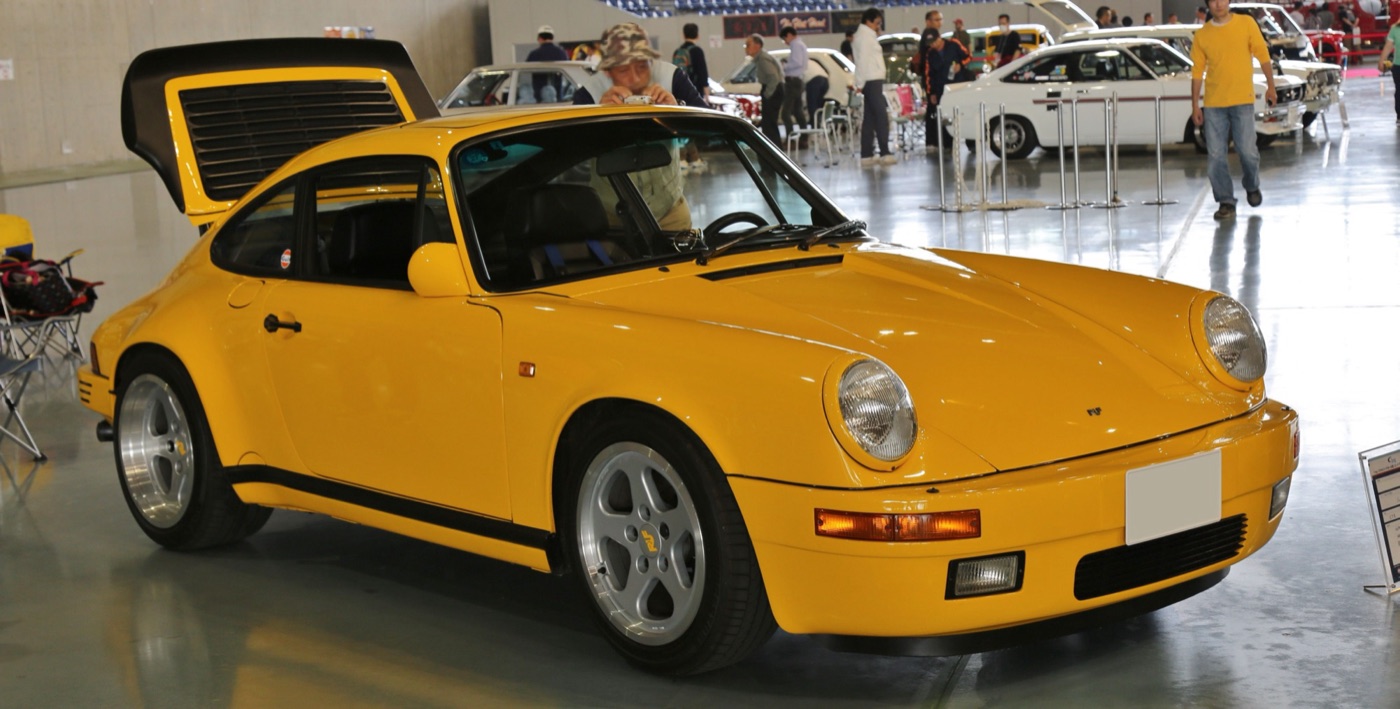 Yellow 1989 Ruf CTR Yellowbird with five-spoke wheels and its rear wing raised, at an indoor car show