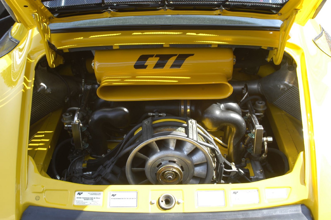 Engine bay of a yellow Ruf CTR with the CTR-lettered intake box over the cooling fan