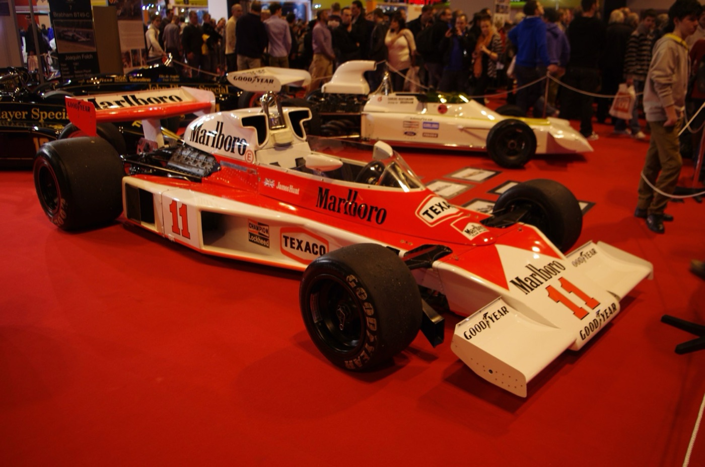 Red and white Marlboro McLaren M23 number 11 with James Hunt’s name on the cockpit side, on a red carpet at a car show