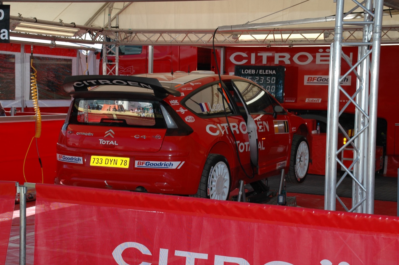 Red Citroën C4 WRC rally car with French registration 733 DYN 78 in a Citroën service tent, its timing board reading Loeb / Elena