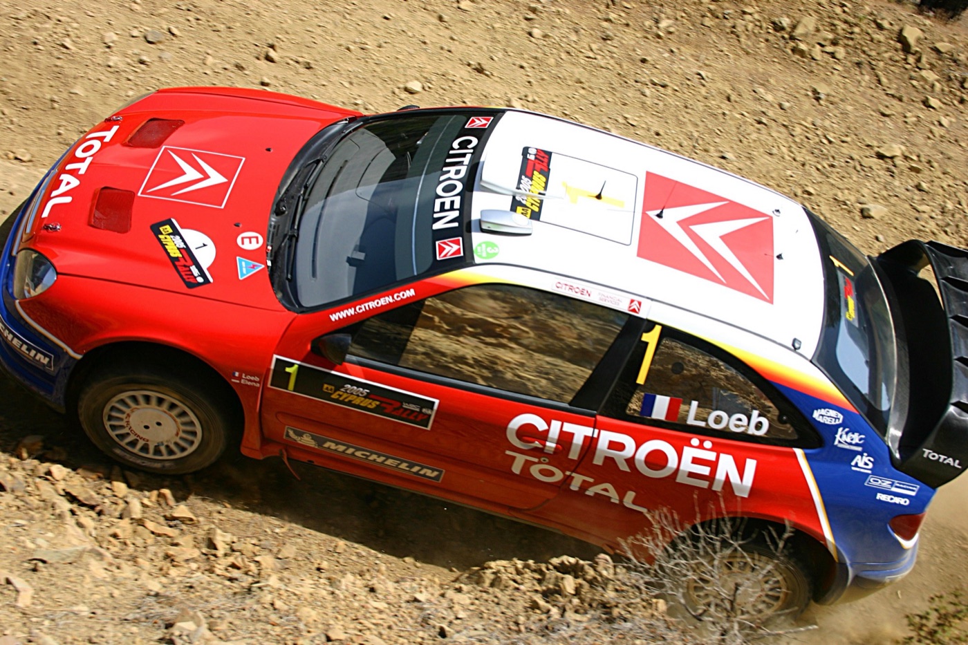 Red, white and blue Citroën Xsara WRC with Loeb’s name on the window, seen from above on a rocky gravel road