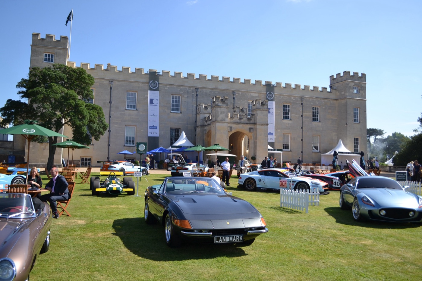Sports cars, a Formula One car and racing GTs on the lawn in front of the battlemented front of Syon House, with green parasols and Salon Privé banners