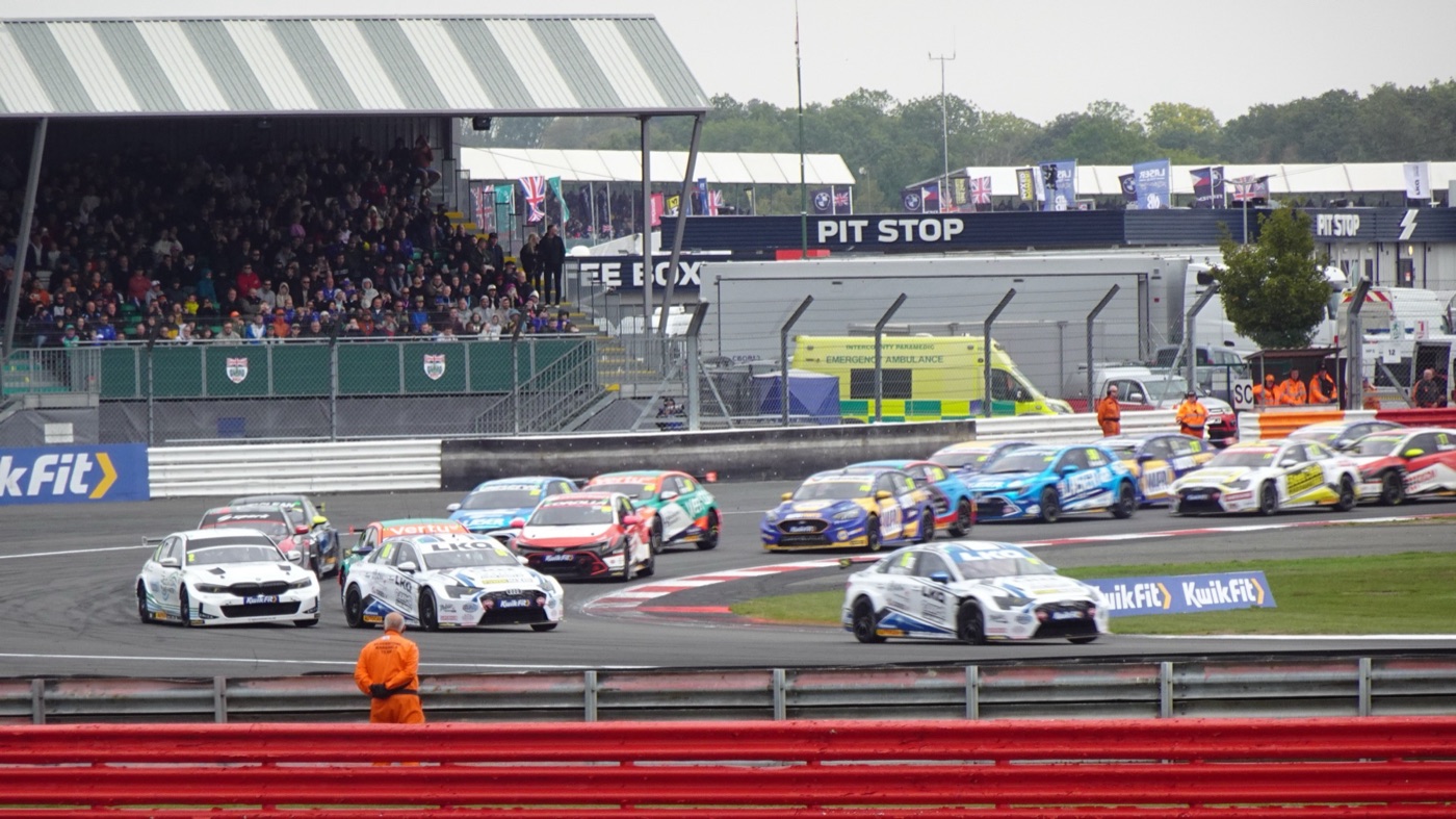 A pack of British Touring Car Championship saloons and hatchbacks bunched through Brooklands corner on the opening lap, with a grandstand behind