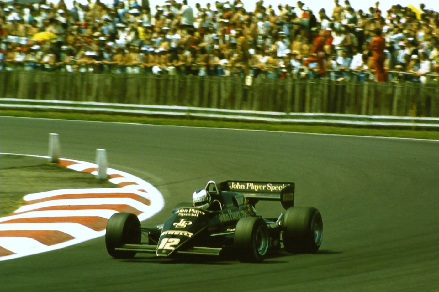 Black and gold Lotus 94T number 12 turning into Copse corner past red and white kerbs, with a packed bank of spectators behind a fence