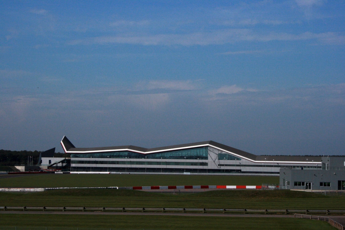 The Silverstone Wing, a long grey and glass pit building with a pointed wing-shaped roof line, seen across grass and the circuit