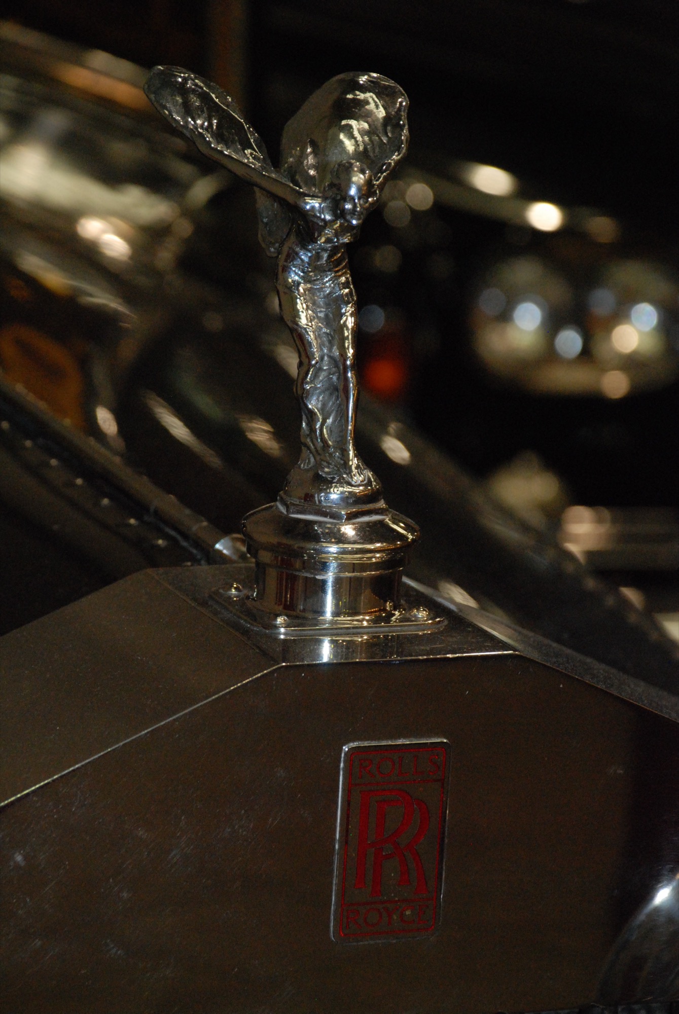 Inter-war Spirit of Ecstasy on the radiator cap of a Rolls-Royce with a red RR badge, in a dimly lit museum hall