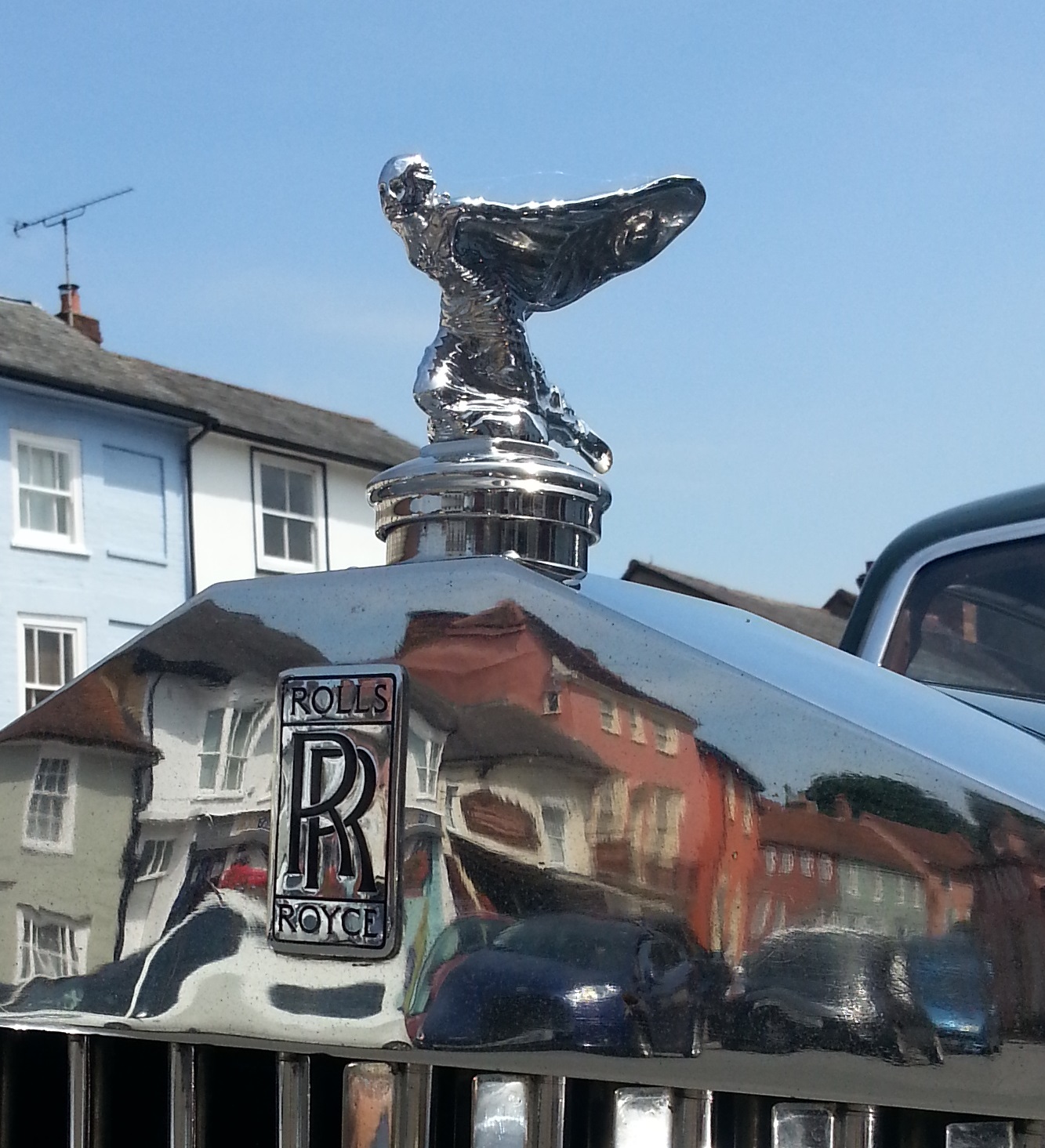 Kneeling Spirit of Ecstasy with swept-back robes above a black and chrome Rolls-Royce badge