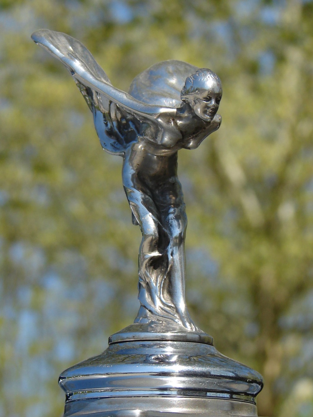 Post-war standing Spirit of Ecstasy seen from the side against trees, on the chromed cap of a Silver Cloud I